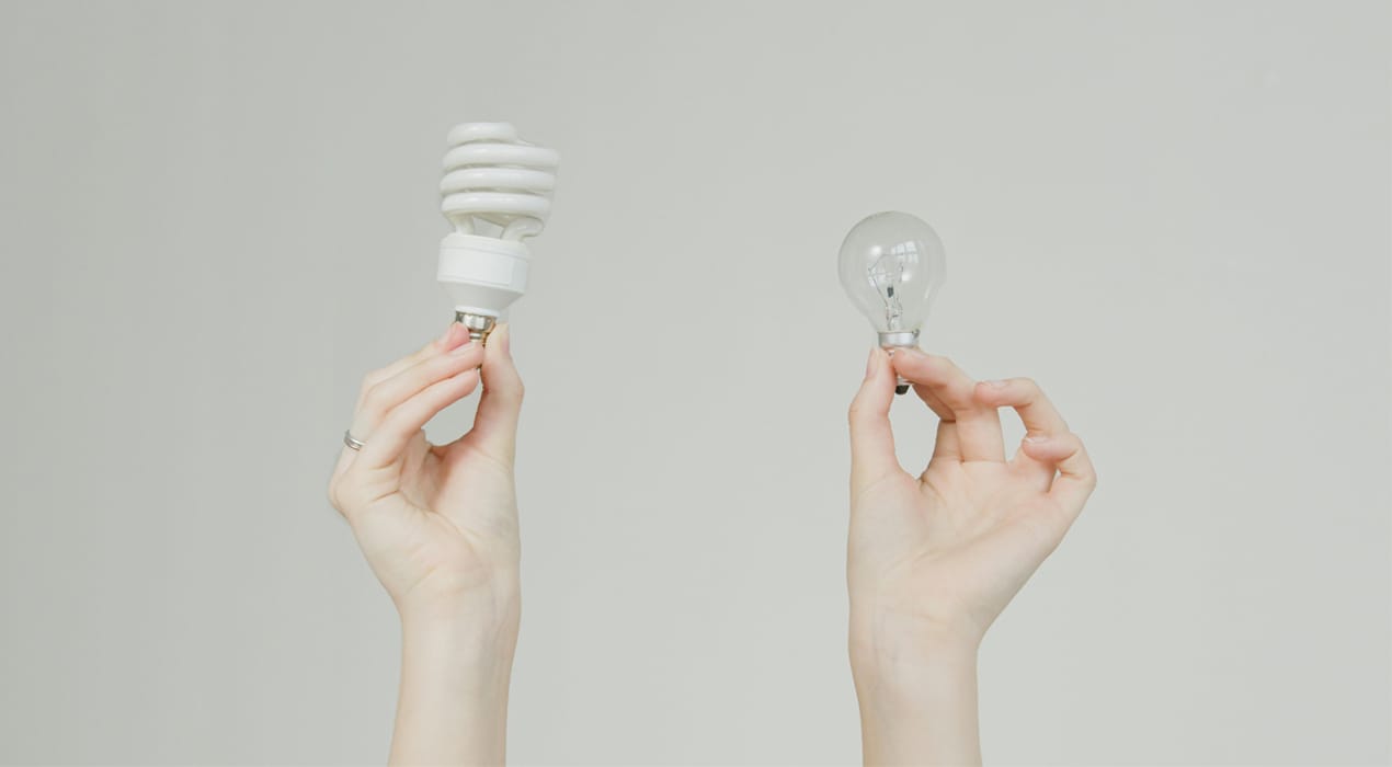 Two hands side by side, one holding a standard lightbulb and one holding an energy-saving lightbulb