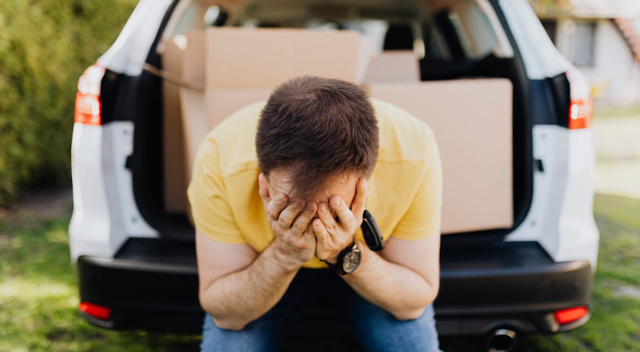 Man sitting in an open car boot with his head in his hands.